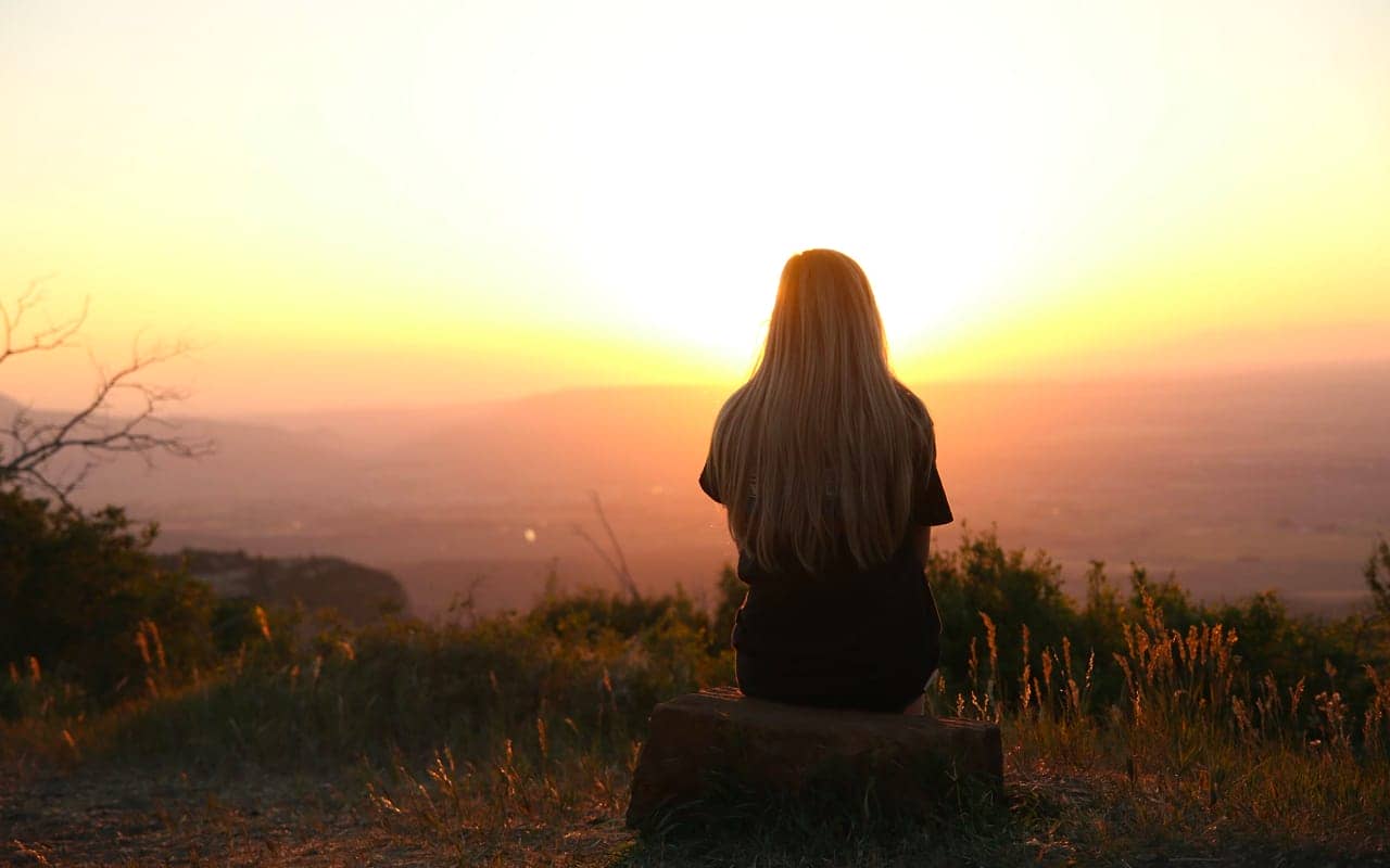 a woman is sitting on a rock enjoying the mountain view