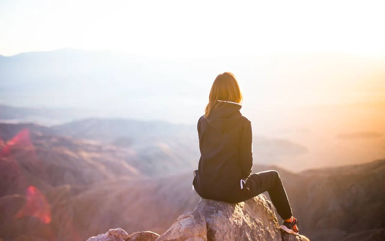 a woman is sitting on a rock with mountain view