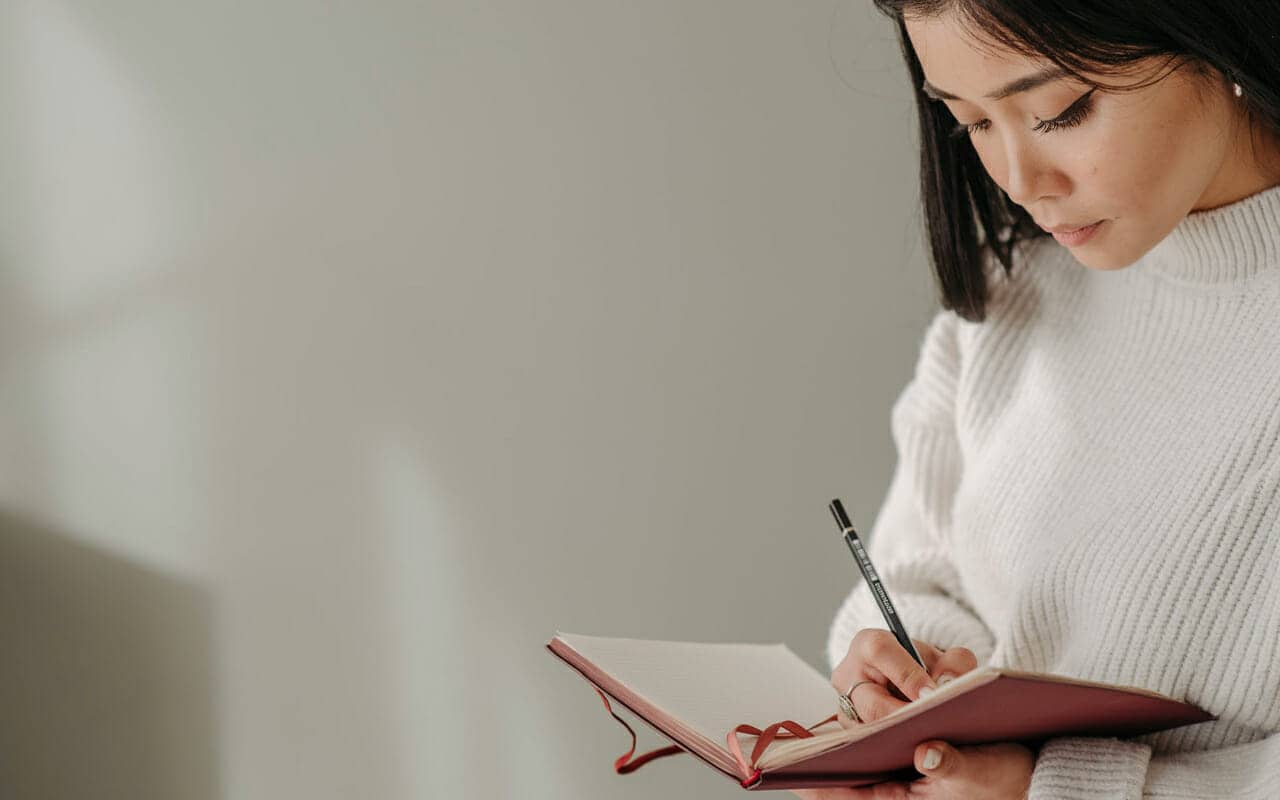 a woman is writing notes on a pink note book