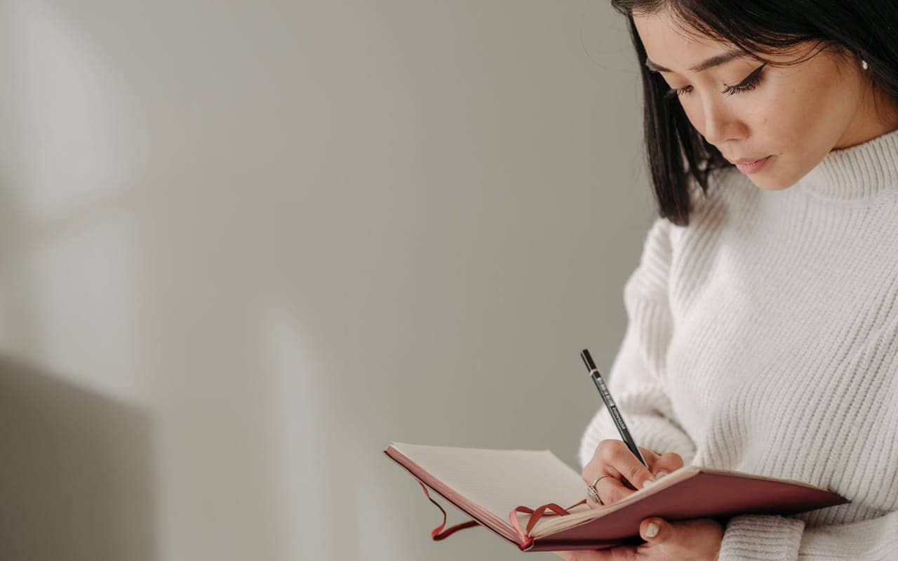 a woman is writing on a pink book