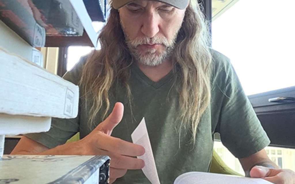 Anthony Metivier reading in a library with a pile of books