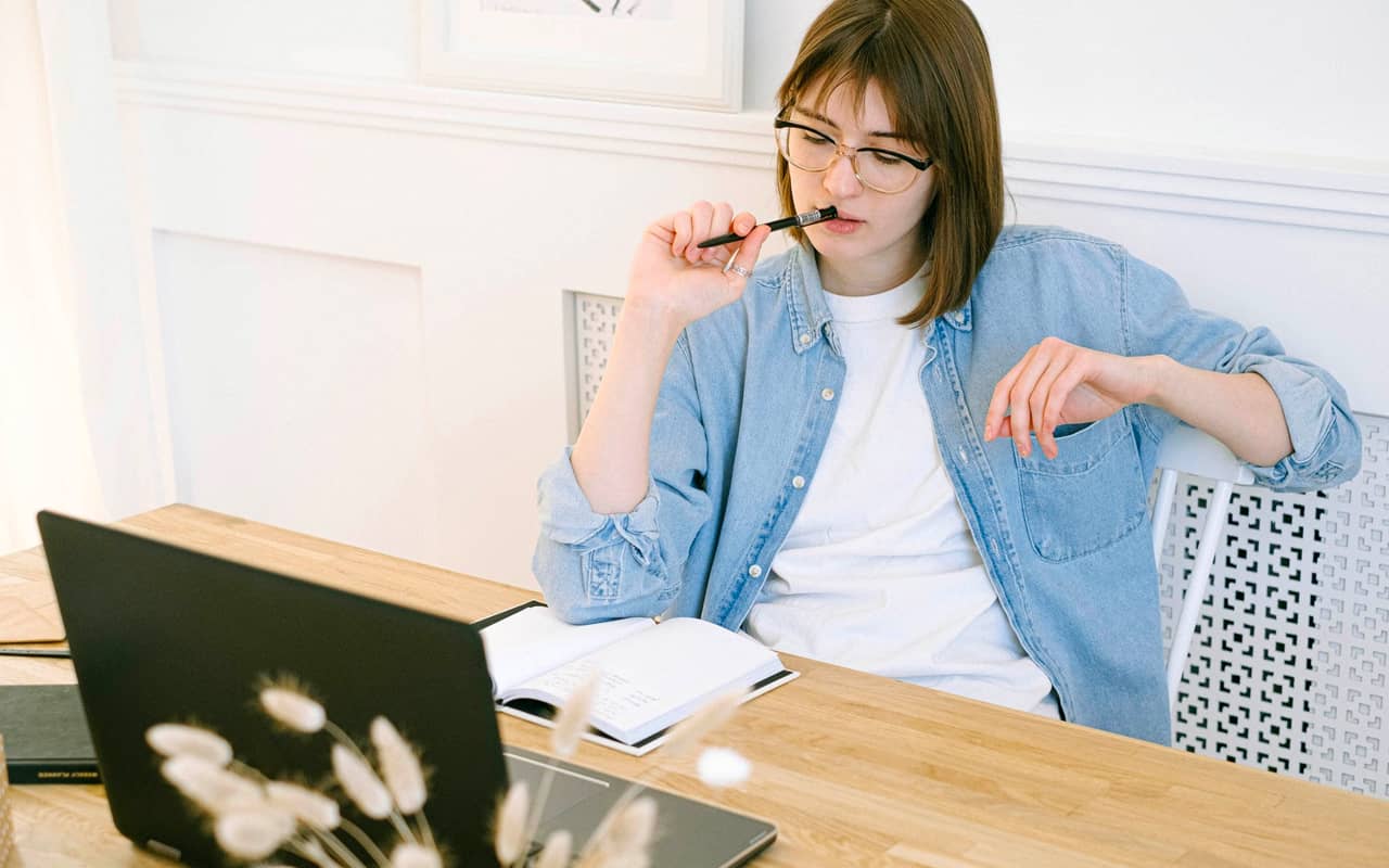 blue shirt woman thinking and writing on her notebook