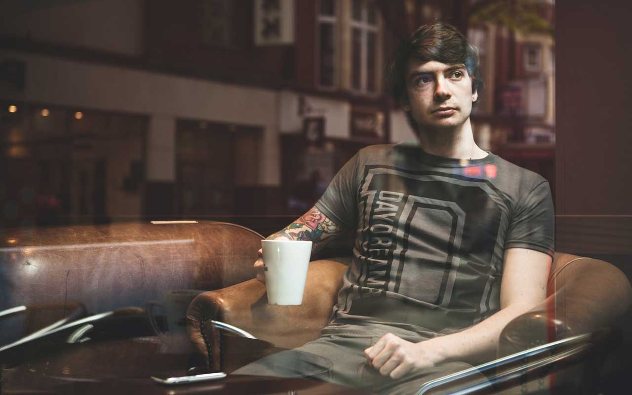 A man daydreams while holding a cup of coffee and staring out the window. His default mode network (DMN) is active.