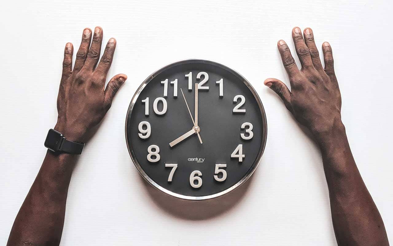 A Black man's hands next to an analog clock.