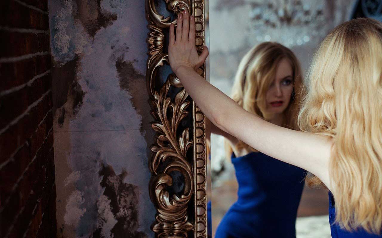 A woman gazes into a mirror, looking at her reflection, much like this mirror guided visualization.