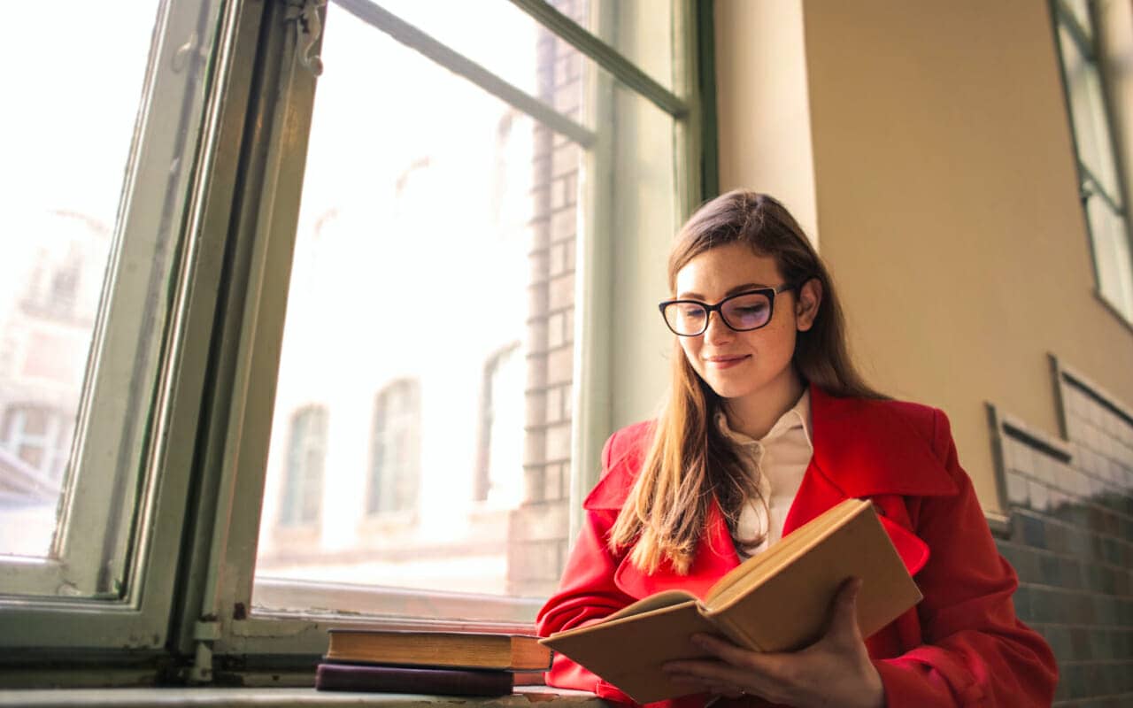 red coat woman is reading beside a window
