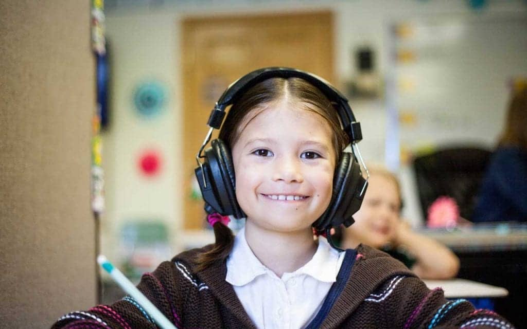A young girl with headphones on smiles at the camera.