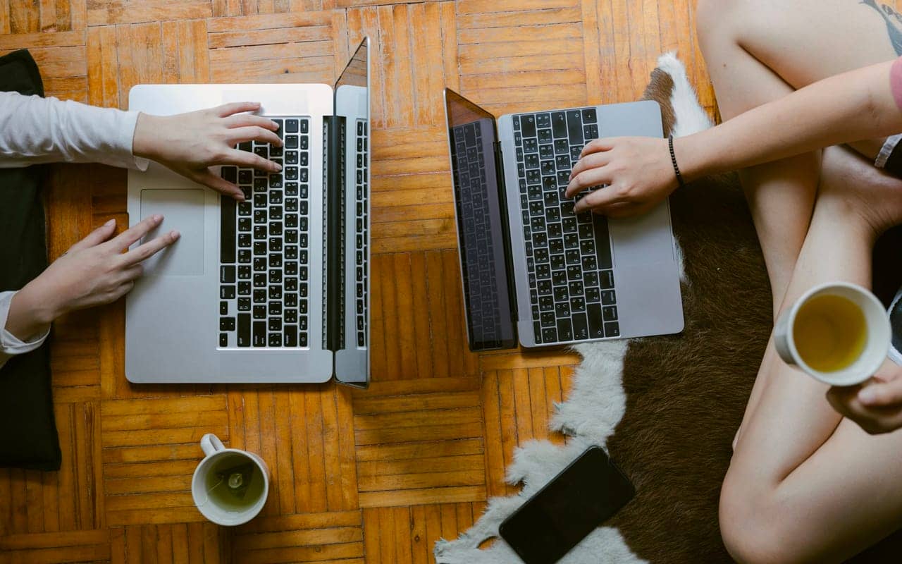 two people are searching on their laptop and drinking tea